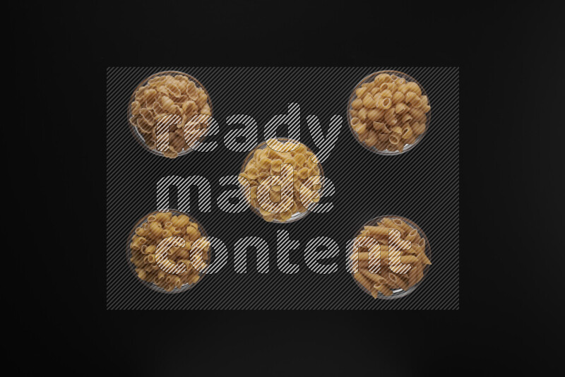 Different pasta types in 5 glass bowls on black background