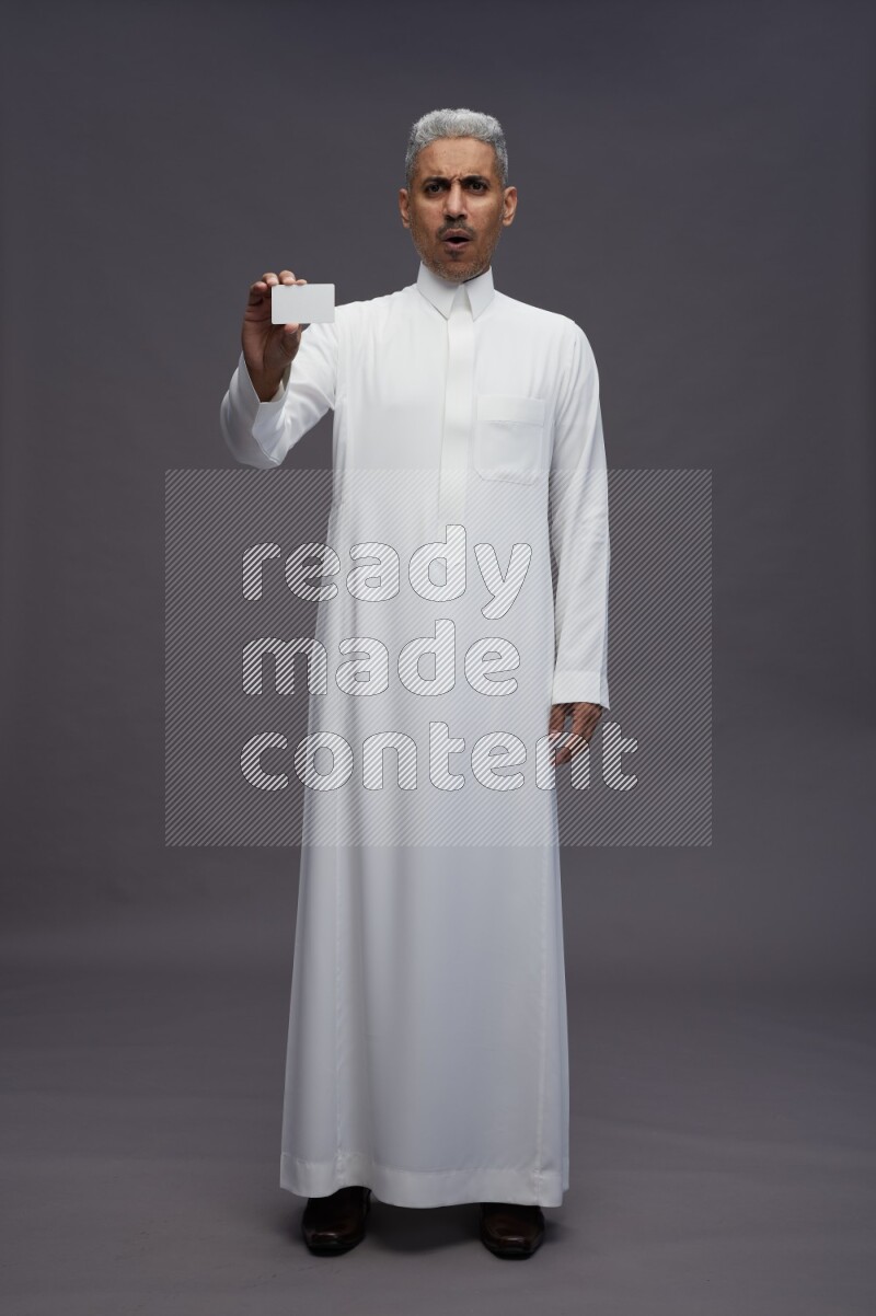 Saudi man wearing thob standing holding ATM card on gray background