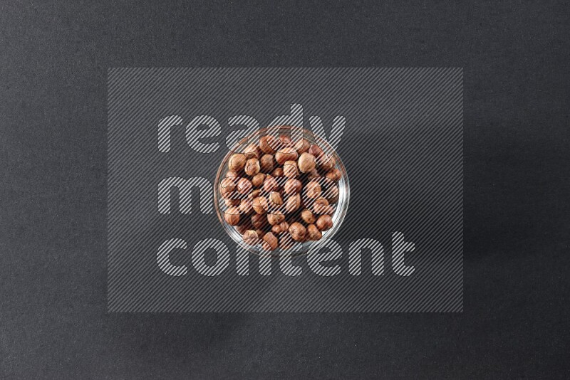 A glass bowl full of peeled hazelnuts on a black background in different angles