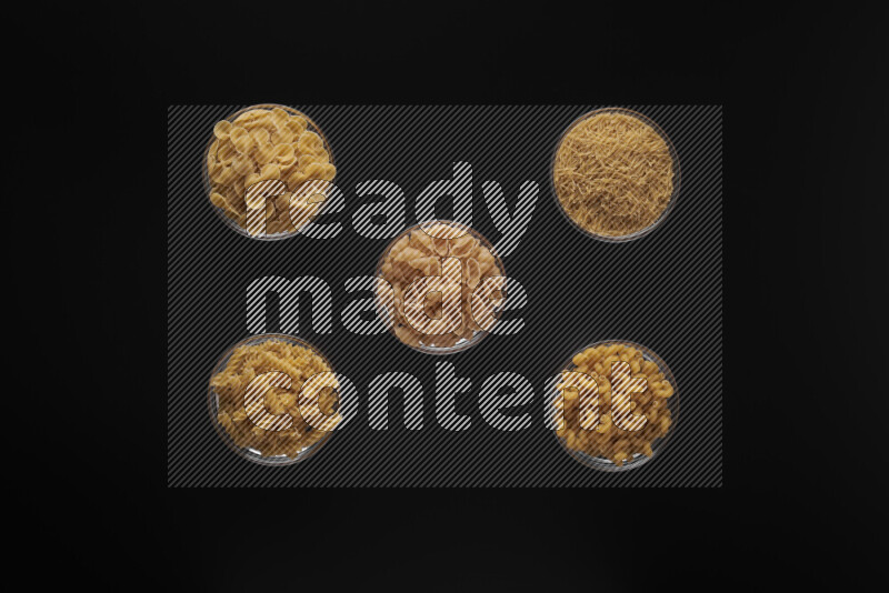 Different pasta types in 5 glass bowls on black background
