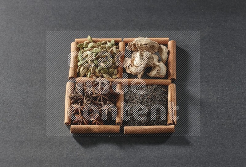 4 مربعات من عيدان القرفة ممتلئة بالشاي واليانسون النجمي والزنجبيل المجفف وحب الهيل على أرضية سوداء