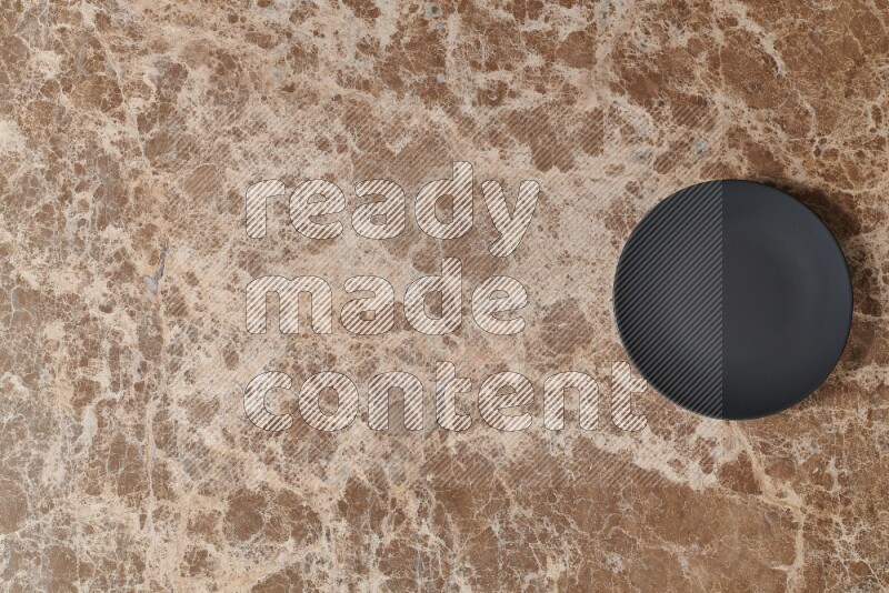 Top View Shot Of A Black Ceramic Circular Plate On beige Marble Flooring