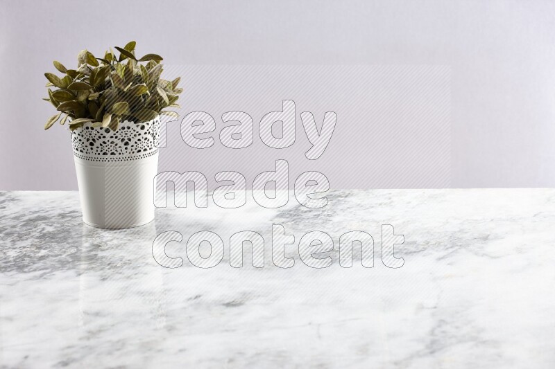 Green artificial plant in white decorative pot on grey marble background