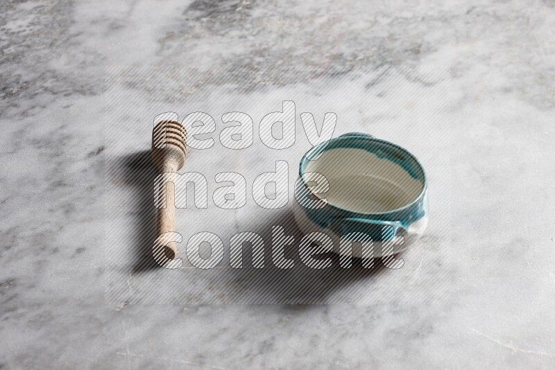 Multicolored pottery bowl with wooden honey dipper on the side on grey marble background