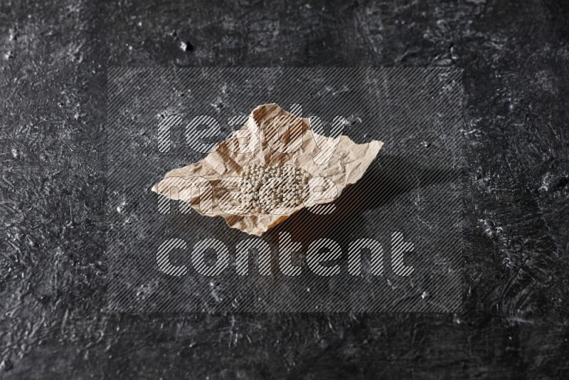 White pepper beads in a crumpled piece of on textured black flooring