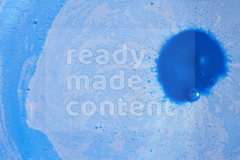 The image captures a dramatic splatter of blue paint over a blue backdrop