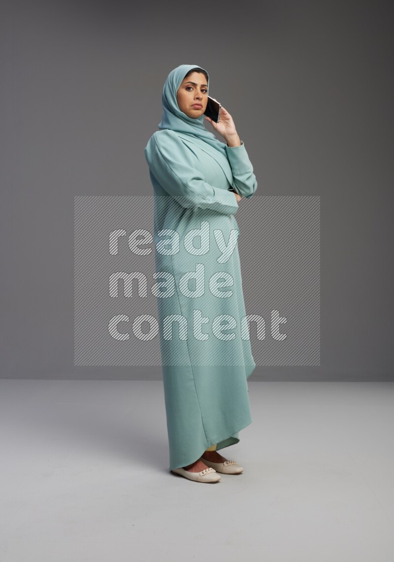 Saudi Woman wearing Abaya standing talking on phone on Gray background