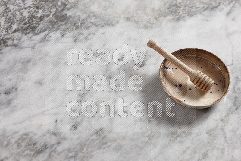 Multicolored pottery bowl with wooden honey dipper in it on grey marble background