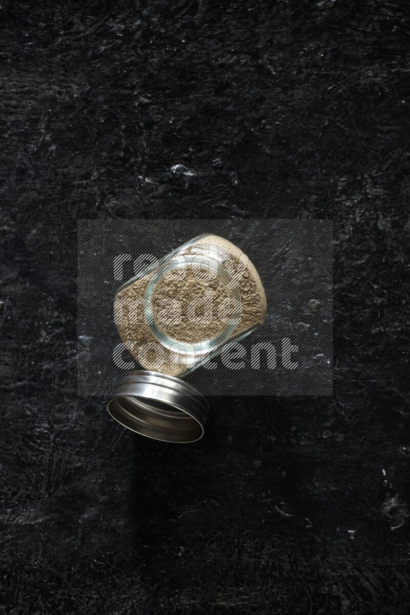 وعاء زجاجي للتوابل ممتلئ ببودرة الهيل على خلفية سوداء