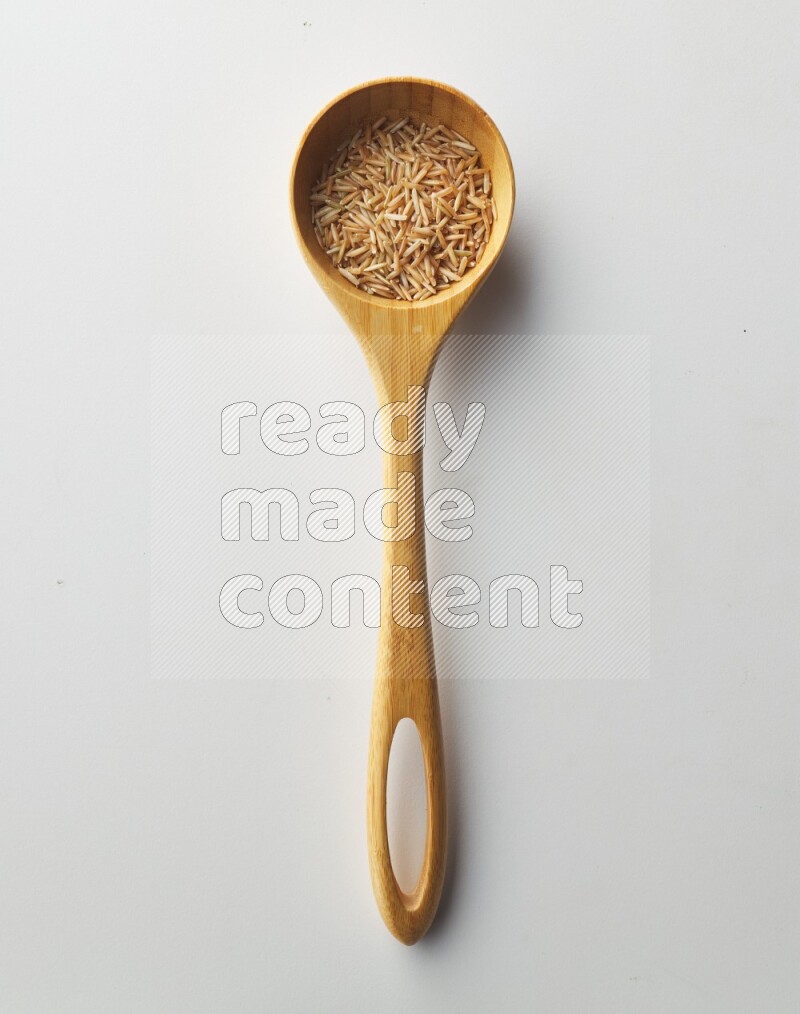 Top-view of a long grain brown rice inside a wooden spoon on white background