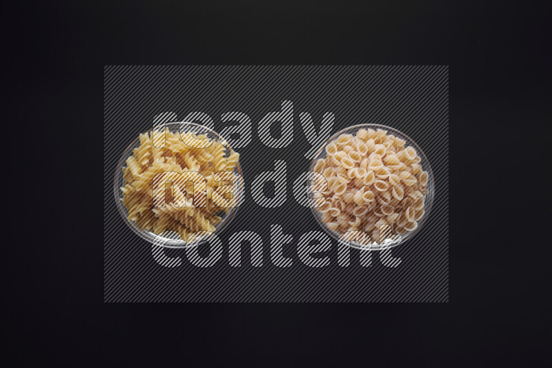 Different pasta types in glass bowls on black background