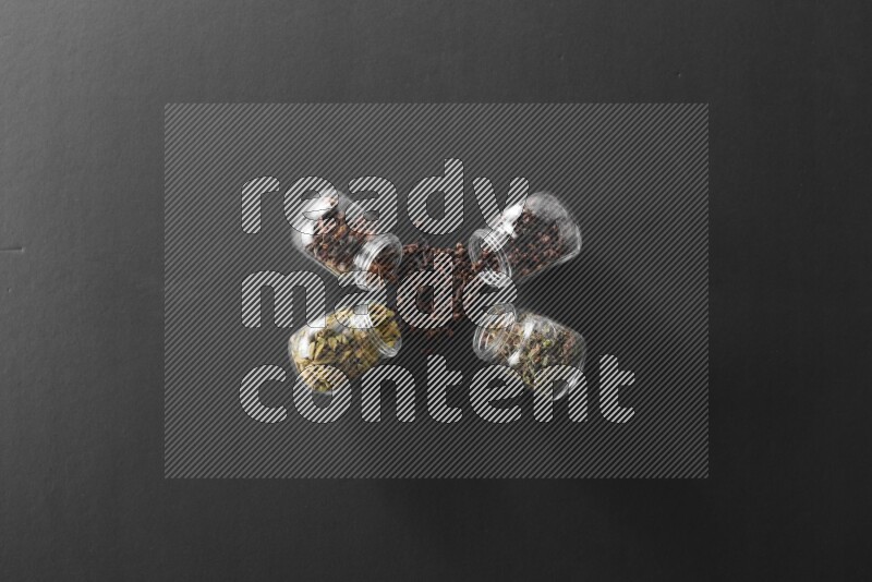 قرنفل وحبوب الهيل وريحان مجفف ويانسون نجمي في أوعية زجاجية علي خلفية سوداء