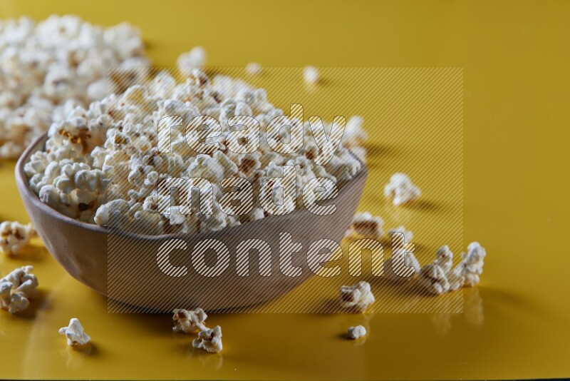 A brown pottery bowl full of popcorn with popcorn beside it on a yellow background in different angles