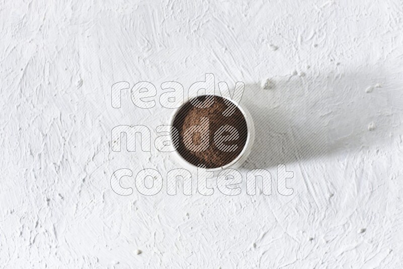 A beige ceramic bowl full of cloves powder on a white flooring