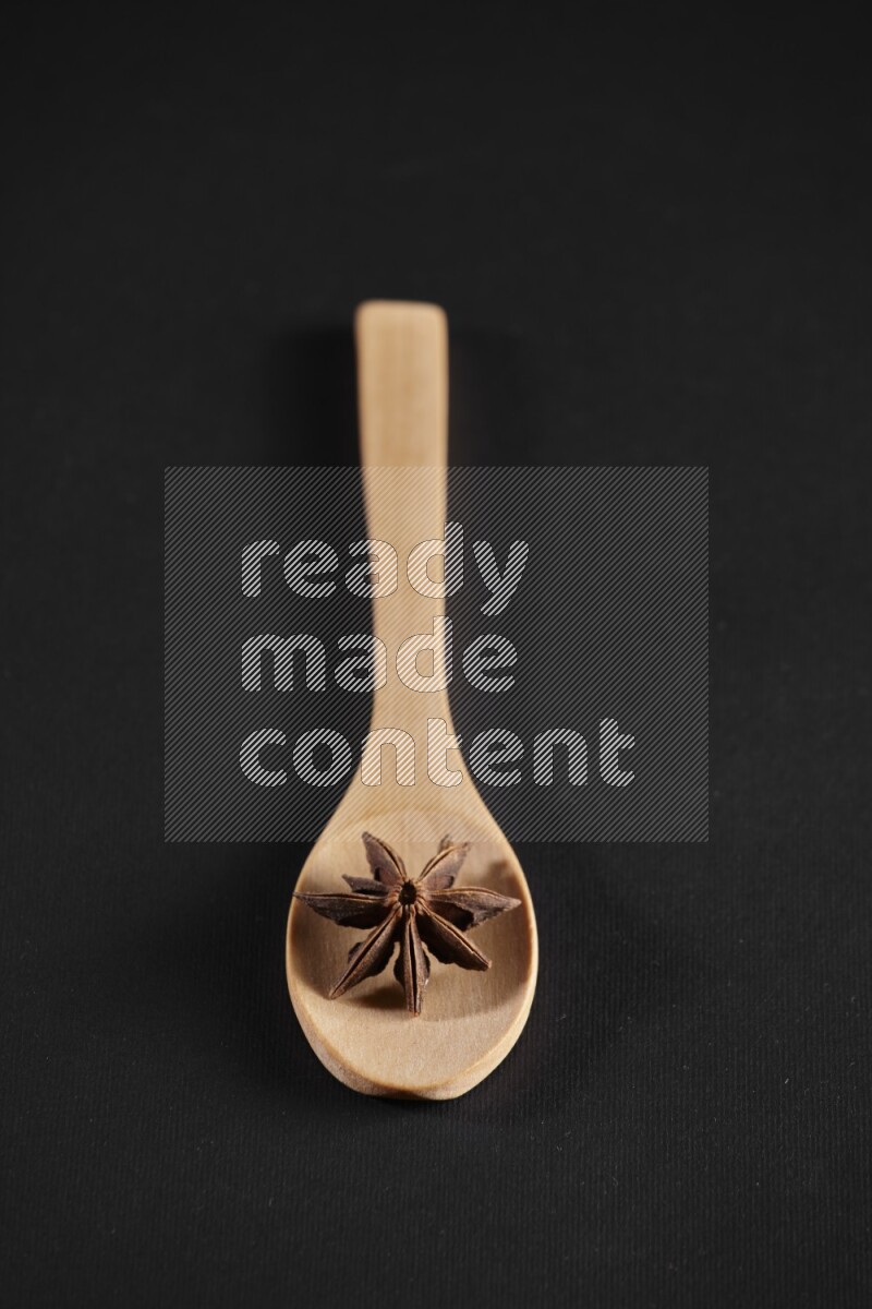 Star Anise in a wooden spoon on more stars anise filling the frame on black flooring