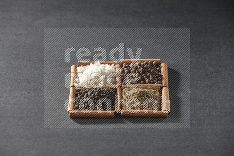 4 مربعات من عيدان القرفة ممتلئة بحبوب الفلفل الأسود والكمون وبهار الفلفل الحلو والملح الأبيض على أرضية سوداء