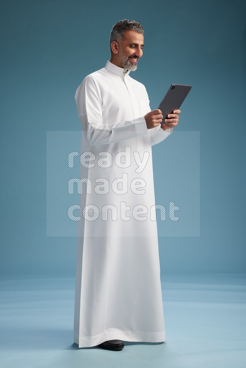 Saudi man waring thob with tablet on blue background