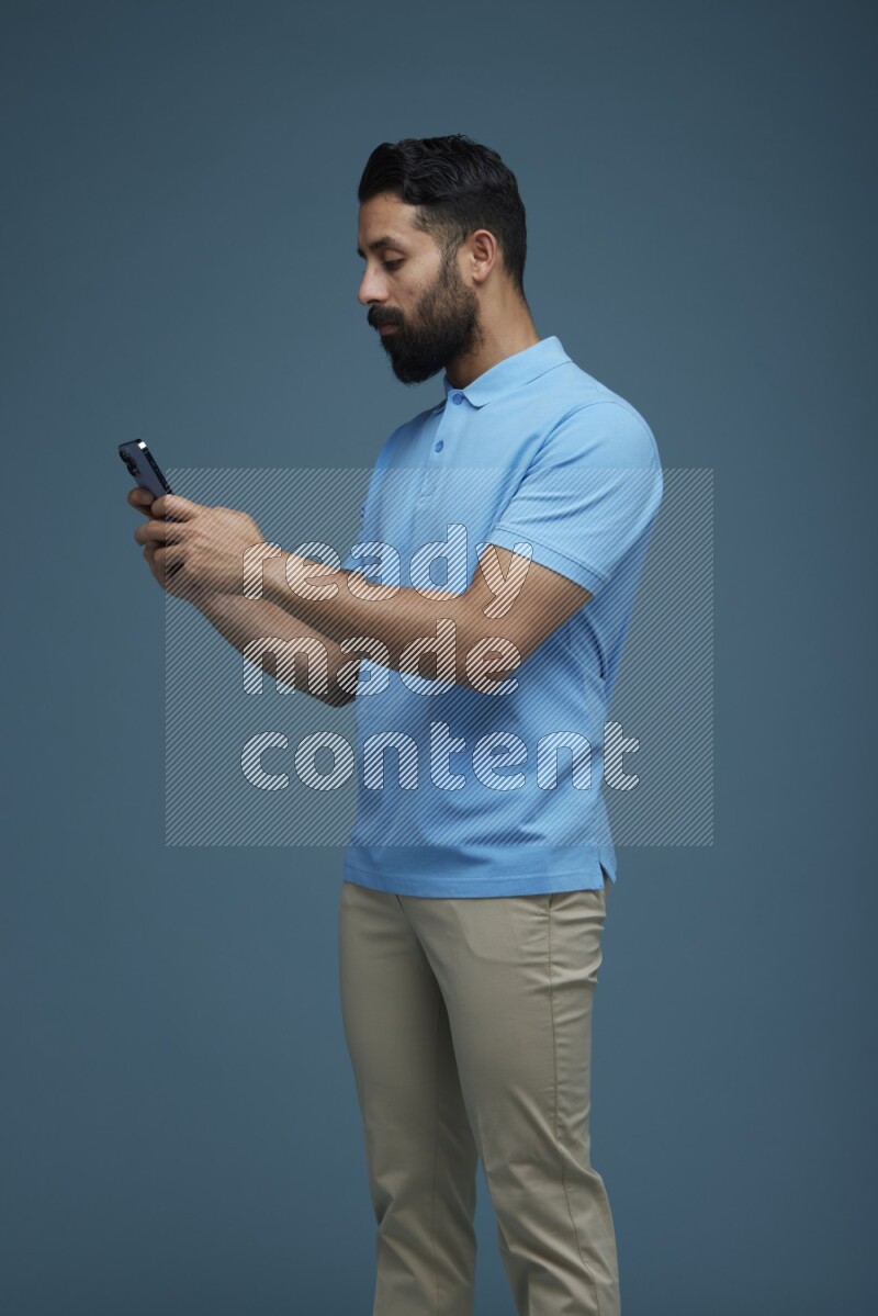 A man Texting on his phone in a blue background wearing a Blue shirt