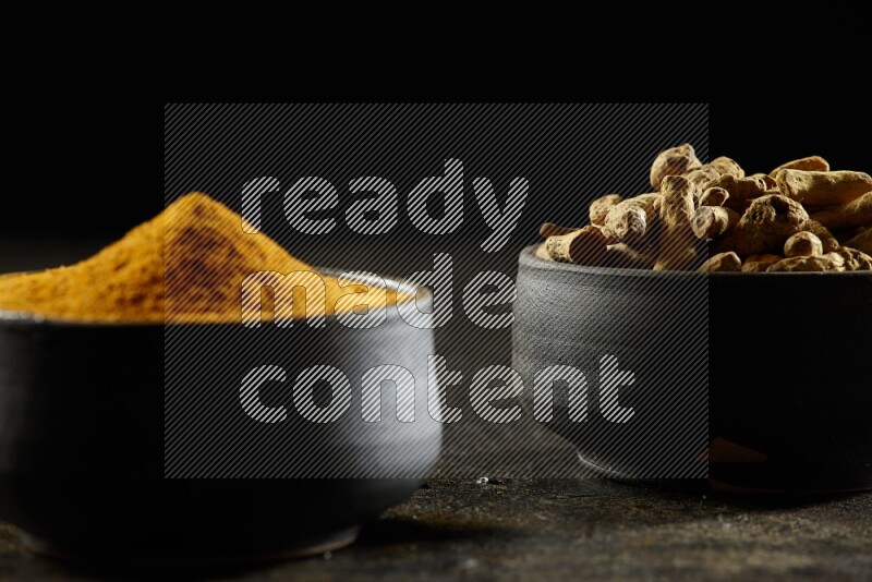 وعاءان من الفخار باللون الأسود، أحدهما ممتلئ ببودرة الكركم والآخر ممتلئ بأصابع كاملة من الكركم المجفف على خلفية سوداء