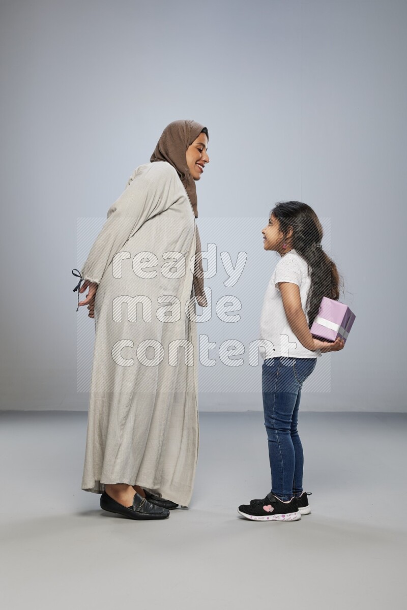 A girl standing hiding a gift behind her back for her mother on gray background