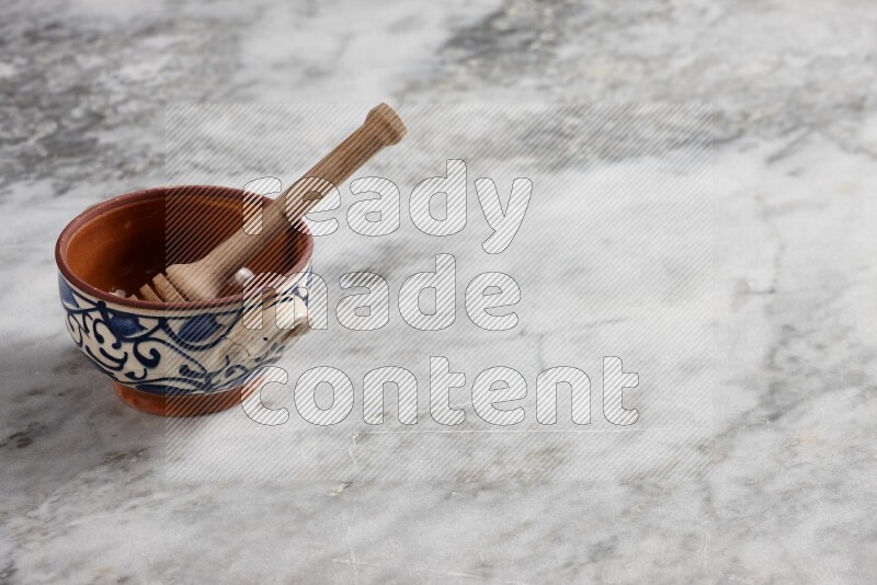 Decorative pottery pot with wooden honey dipper in it on grey marble background