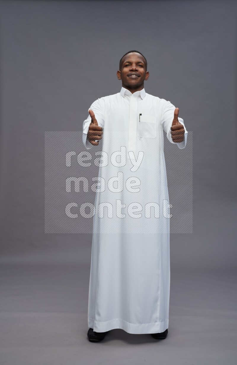 Saudi man wearing thob standing interacting with the camera on gray background
