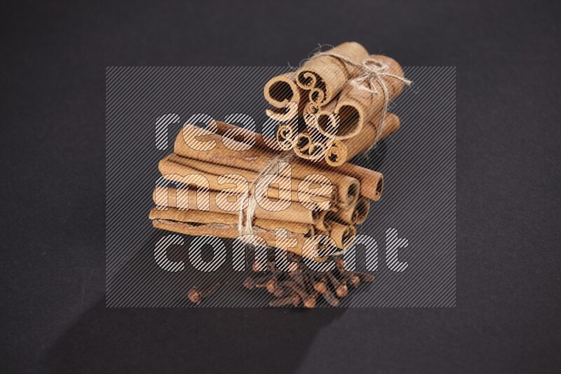 Two bounded stacks of cinnamon sticks with cloves on black background