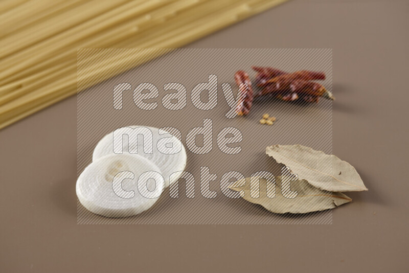 Raw pasta with different ingredients such as cherry tomatoes, garlic, onions, red chilis, black pepper, white pepper, bay laurel leaves, rosemary and cardamom on beige background