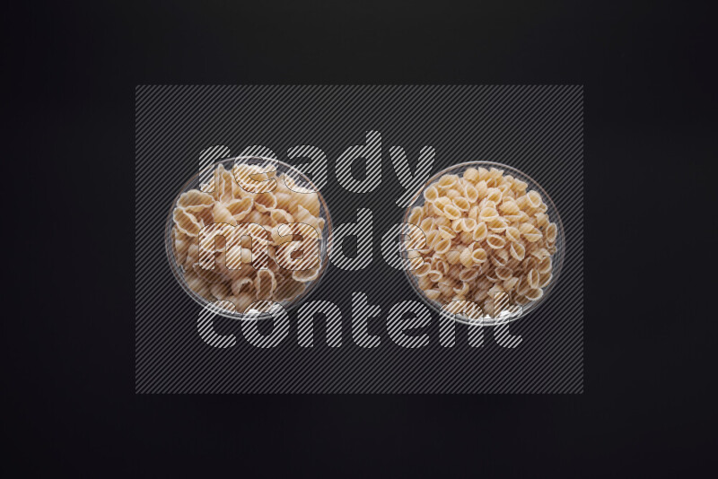 Different pasta types in glass bowls on black background