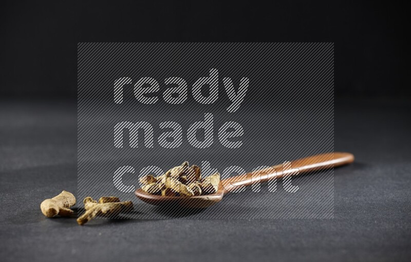A wooden ladle full of dried turmeric fingers on black flooring