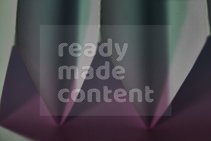 صورة مجردة مقربة تظهر طيات ورقية هندسية حادة بتدرجات اللون الأخضر والوردي