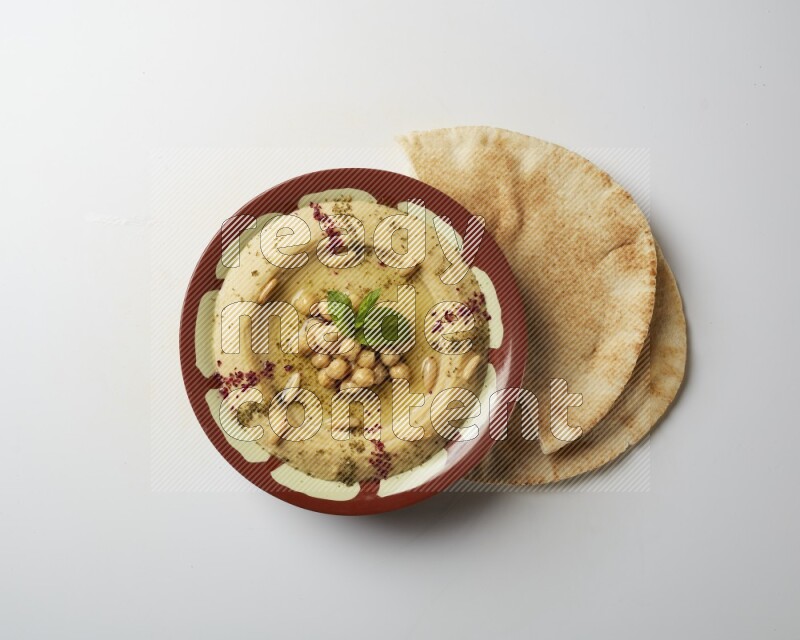 Hummus in a traditional plate garnished with zaatar & sumak on a white background