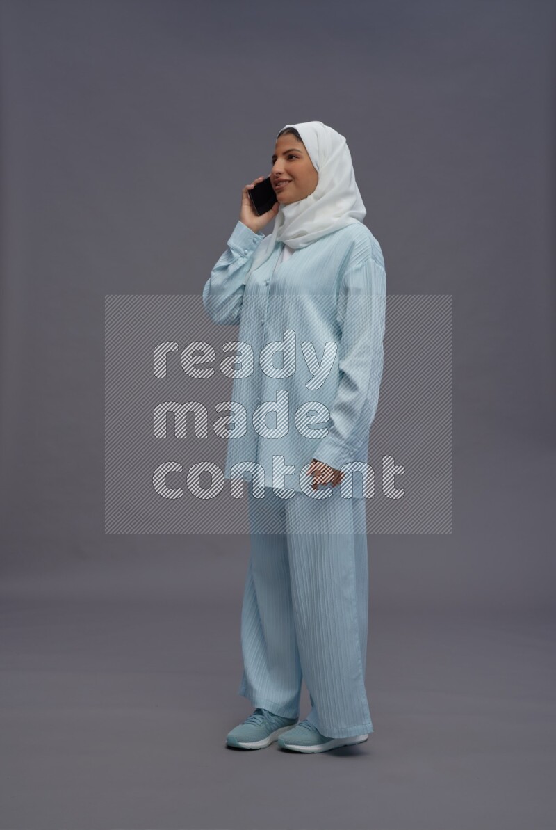 Saudi woman wearing hijab clothes standing talking on phone on gray background