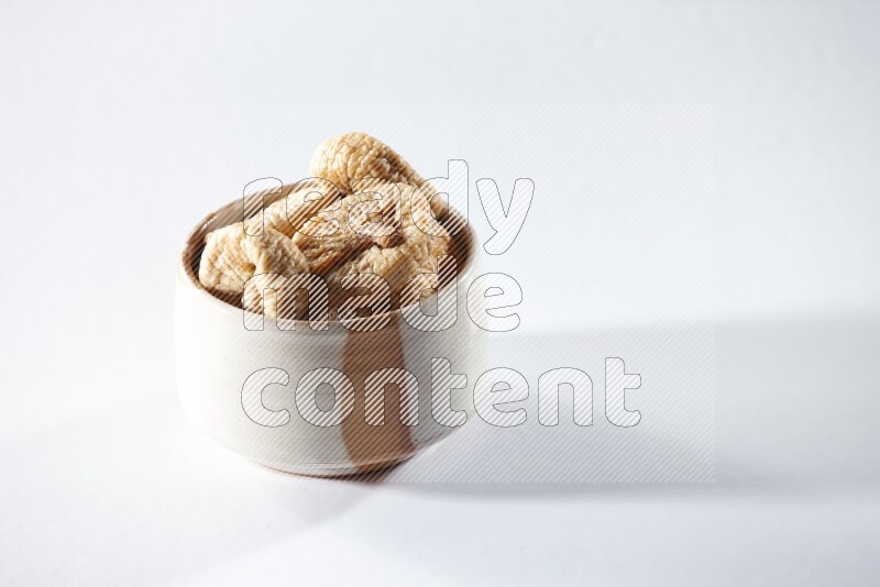 A beige ceramic bowl full of dried figs on a white background in different angles