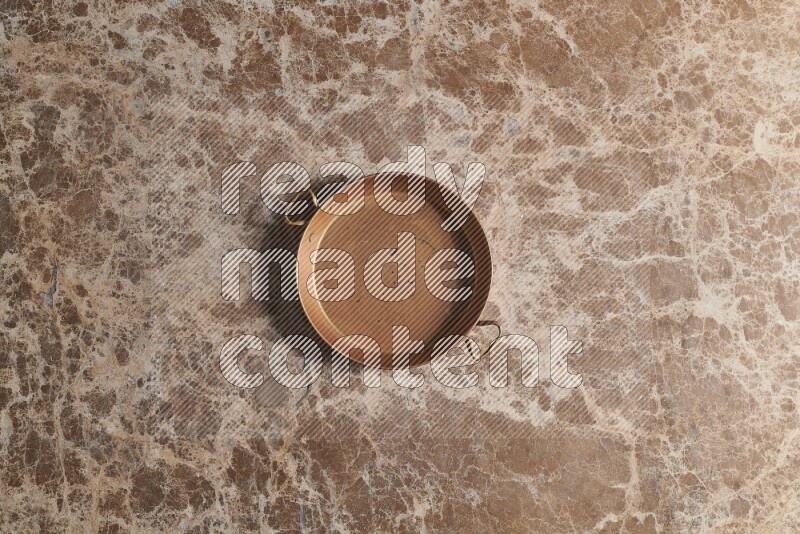 A small copper pan on beige marble background