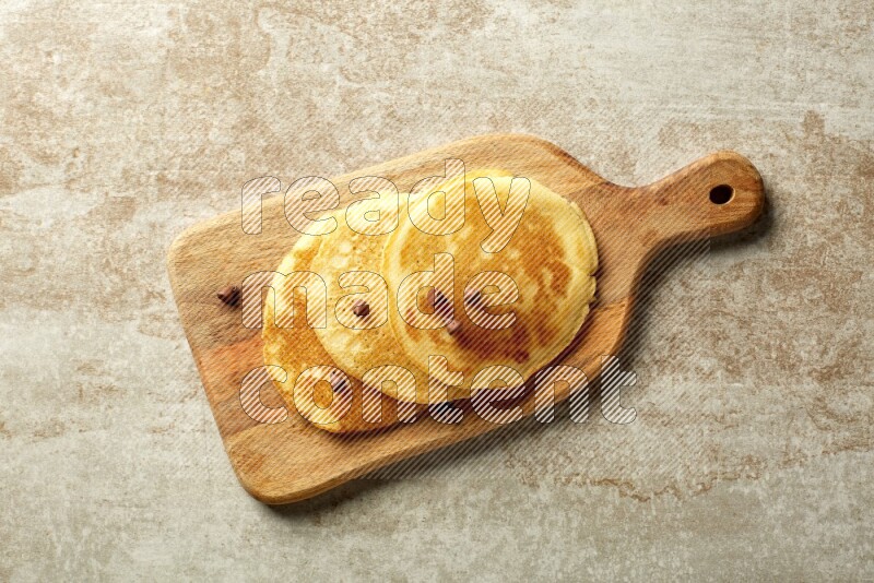 Three stacked chocolate chips pancakes on a wooden board on beige background