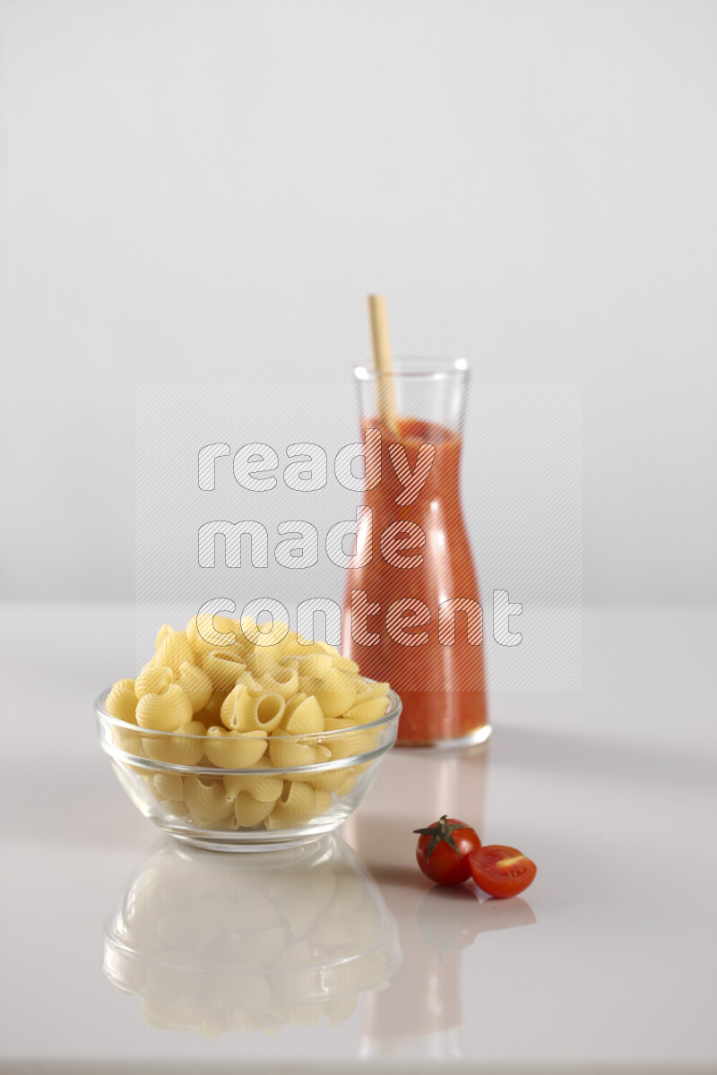 Raw pasta with tomatoe pasta with different ingredients such as cherry tomatoes, basil, garlic, bay laurel, cardamom, white pepper, black pepper, red chilis and wheat stalks on light grey background