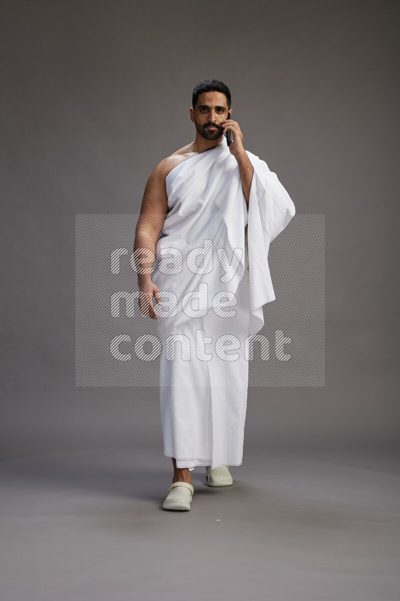 A man wearing Ehram Standing talking on phone on gray background