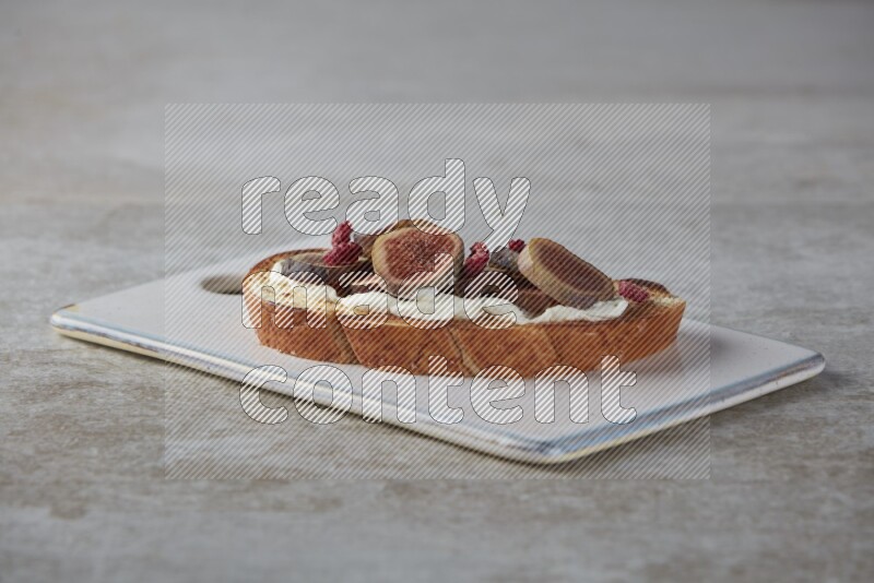 figs slices  with cream cheese on toasted sourdough slice on a wooden board on textured grey background