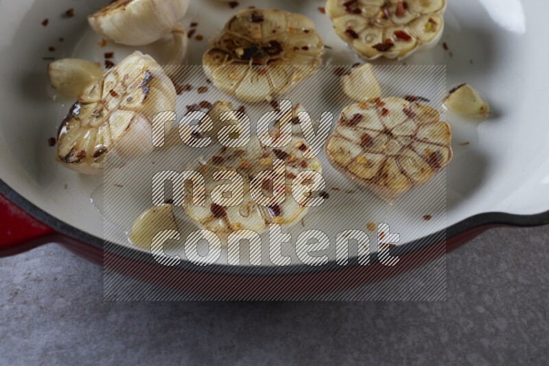 half's roasted garlic in a red-coated cast iron pan on a grey textured countertop