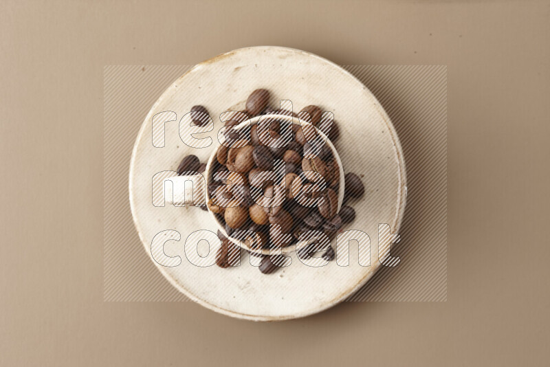 A beige pottery cup full of roasted coffee beans on beige background