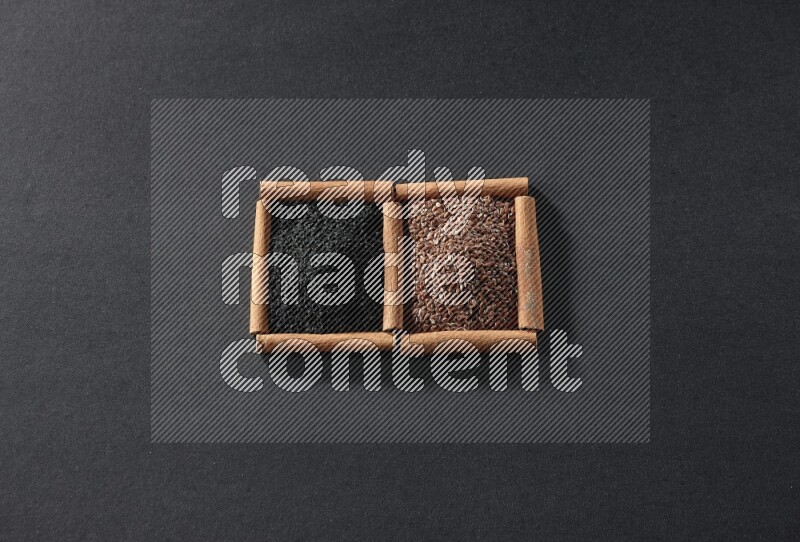 2 squares of cinnamon sticks full of flaxseeds and black seeds on black flooring