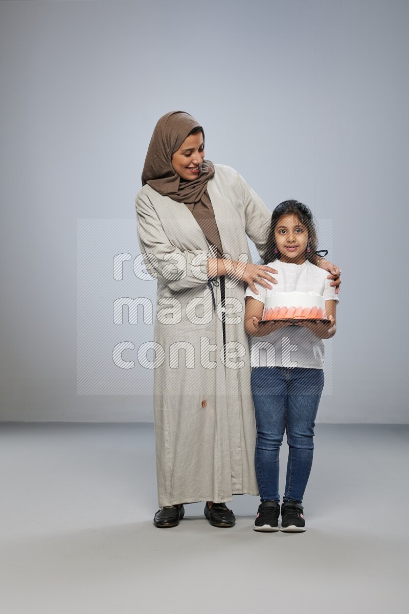 A girl giving a cake to her mother on gray background