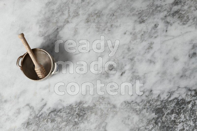 Multicolored pottery bowl with wooden honey dipper in it on grey marble background