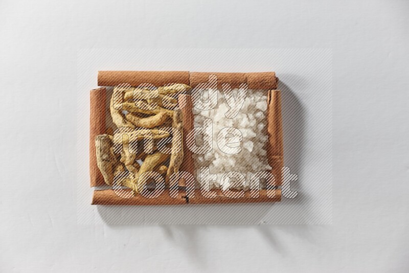 2 squares of cinnamon sticks full of turmeric fingers and white salt on white flooring