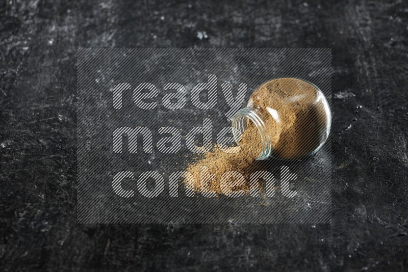 وعاء زجاجي مقلوب ممتلئ ببودرة الكمون والبودرة تناثرت منه على خلفية سوداء