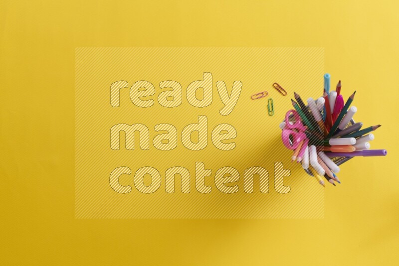 Pens, pencils and school supplies in a metal pen holder on yellow background