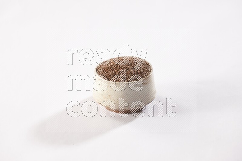 A pottery beige bowl full of flax seeds on a white flooring
