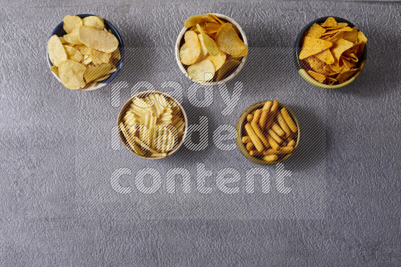 Assorted snacks in pottery bowls on grey background