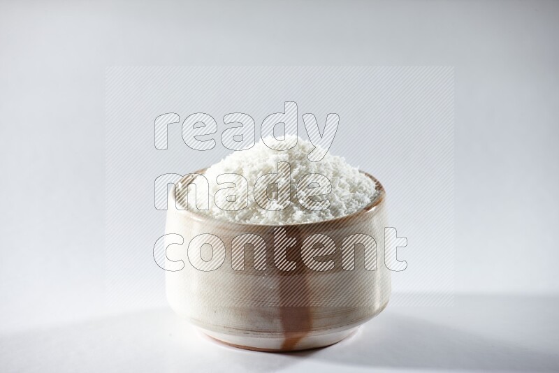 A beige ceramic bowl full of desiccated coconut on a white background in different angles